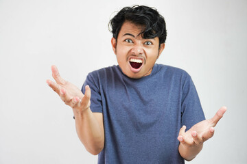 Fototapeta premium Handsome young Asian man wearing casual t-shirt standing over white background and madly screaming and shouting with aggressive expression and raised hands. Frustration concept.