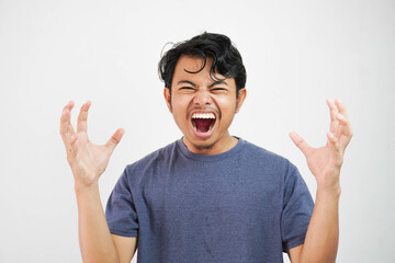 Handsome young Asian man wearing casual t-shirt standing over white background and madly screaming and shouting with aggressive expression and raised hands. Frustration concept.