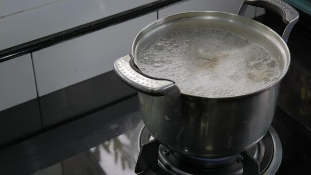 Boiling soup in stainless steel pot over gas stove with meat bubble over hot water.