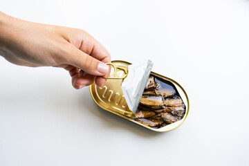 Female hand opening sprats with oil on the white background, close up image