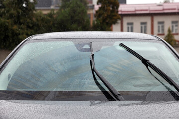 Car wipers cleaning water drops from windshield glass outdoors, closeup