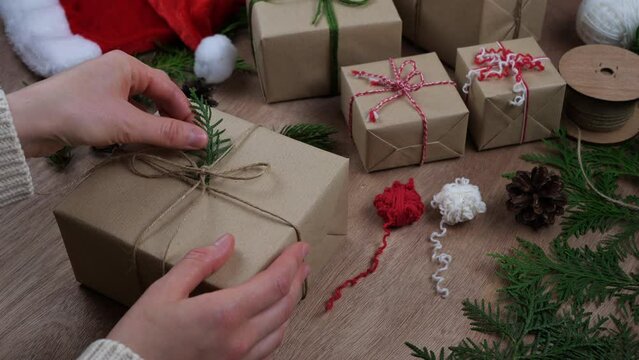 Hands wrap a sustainable Christmas gifts. Eco friendly presents, decoration with twigs. Sustainable gift wrapping. Plastic-free packaging, recycled paper and twine.