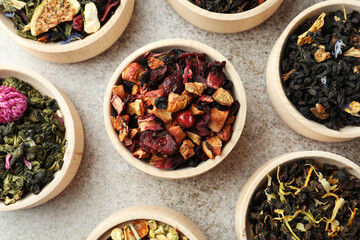 Different kinds of dry herbal tea in wooden bowls on light grey table, flat lay