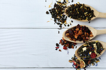 Spoons with dried herbal tea leaves and fruits on white wooden table, flat lay. Space for text