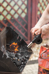 Man's hand holding and using air blower to fire up charcoal in a metal tray, portable grill...