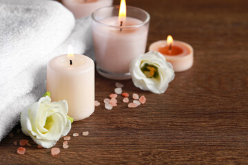 Fototapeta na wymiar Beautiful spa composition with burning candles and flowers on wooden table. Space for text