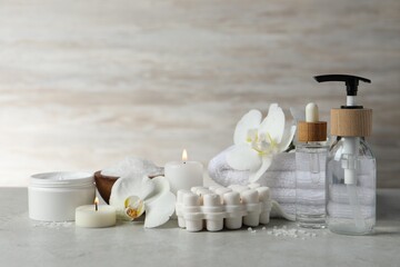 Beautiful composition with different spa products, burning candles and flowers on light grey table. Space for text