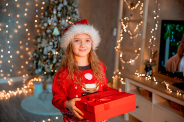 happy little girl holding christmas gift near the christmas tree at home for christmas