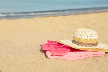 Fototapeta na wymiar Beach towel with straw hat and slippers on sand near sea