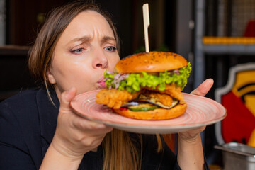Funny shot woman blowing and looking at large hamburger with skewer on plate in restaurant. Beef, pork burger with buns