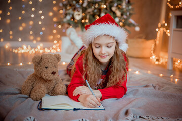 a little girl writes a letter to Santa Claus near the Christmas tree at home for Christmas