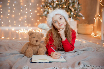 a little girl writes a letter to Santa Claus near the Christmas tree at home for Christmas