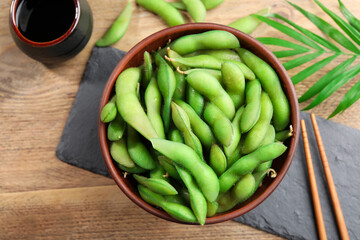 Green edamame beans in pods served with soy sauce on wooden table, flat lay