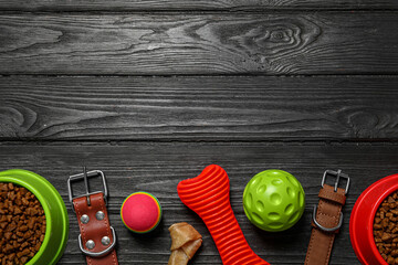 Flat lay composition with dog collars, toys and food on black wooden table. Space for text