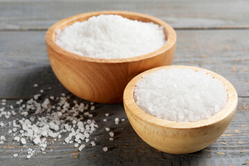 Bowls of natural sea salt on grey wooden table, closeup