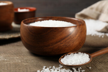 Bowl and spoon with natural sea salt on wooden table, closeup