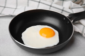 Tasty fried egg in pan on light grey table, closeup