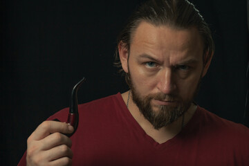 Lumberjack brutal beard muscled man in red shirt with smoking tube pipe standing on dark background