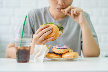 Satisfied Asian woman eating fried chicken burger and french fries. Unhealthy eating concept.