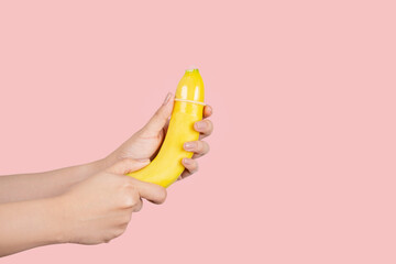 Woman putting condom on banana against color background. Safe sex concept