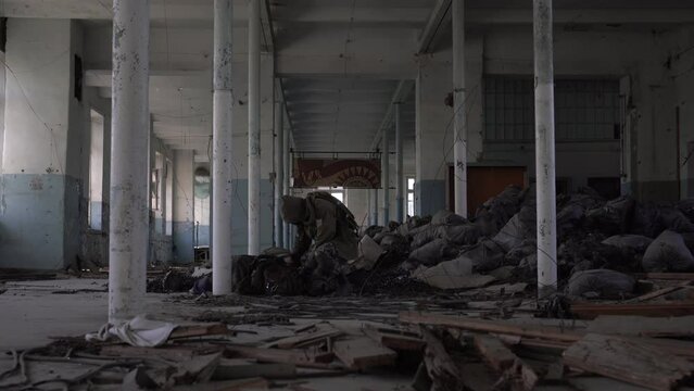 stalker searches the backpack of a dead man in a ruined building. The concept of post-apocalypse and survival after a nuclear winter