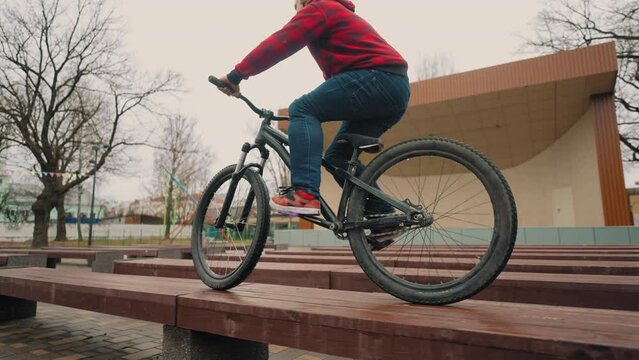 bmx bike tricks in park, teen boy is practicing, training, doing jumps and riding on bench