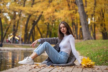 Young brunette girl in blue jeans posing in an autumn park