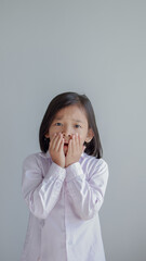 Surprised and shocked screaming asian child covering mouth with her hand. isolated on light grey background.