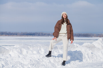 Full length portrait of a young beautiful brunette woman in white trousers and a brown down jacket