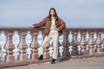 Full length portrait of a young beautiful brunette girl in white trousers and a brown down jacket