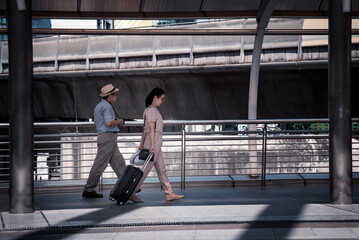 Fototapeta na wymiar Tourist woman and oldest man wearing casual dress ,hand holding baggage for travel walking and talking passed the public sky walk bridge.