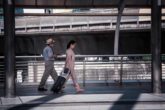 Tourist woman and oldest man wearing casual dress ,hand holding baggage for travel walking and talking passed the public sky walk bridge.