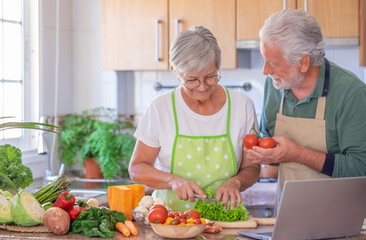 Attractive smiling senior couple working together in home kitchen preparing vegetables enjoying healthy eating.