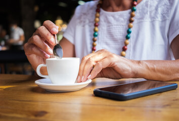 Mature caucasian woman sitting at coffee shop drinking an espresso coffee. Wooden table and smartphone on it