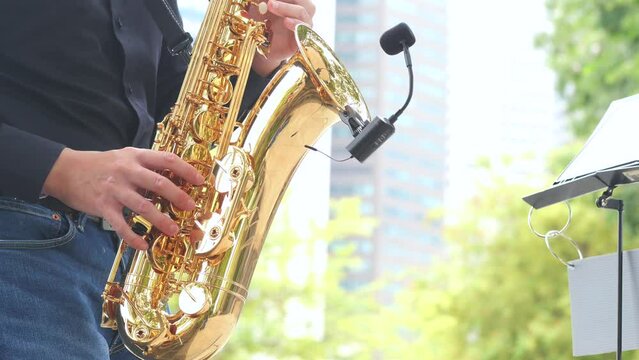 male's hands playing the saxophone outdoors.