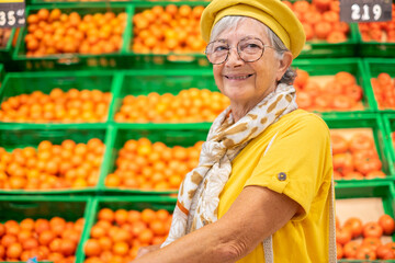 Senior woman in yellow with cap doing purchases in supermarket department, tomatoes in background
