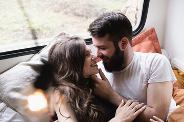 Young just married couple is traveling in travel van. Romantic atmosphere of relaxation. Road trip around country for weekend. Caucasian man and woman lying in bedroom in camper. Millennial generation