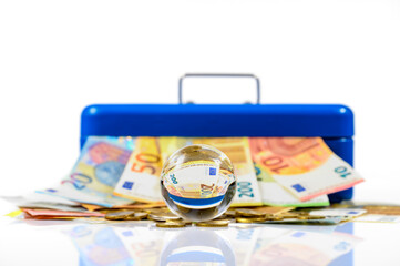 euro bills and coins lying on table and sticking out of blue cash box with reflection in glass ball