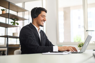 Young man wearing wireless headset using a laptop computer for communication with customers or...