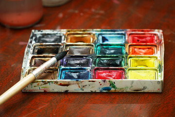Watercolor paints and a brush on the table. Selective focus