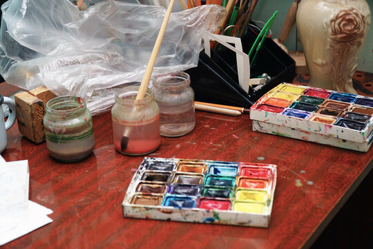 Watercolor paints, a paint brush and jars of water on the table. Selective focus