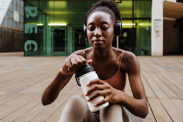 Obraz premium Young beautiful african woman in headphones opening bottle of water
