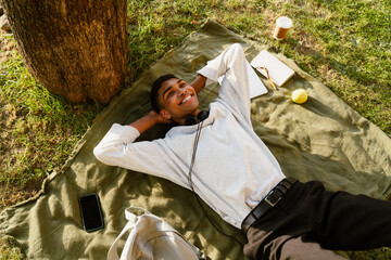 Young black man smiling while lying on blanket under tree in park
