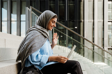 Young muslim woman wearing headscarf using laptop while sitting outdoor