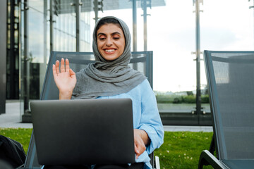 Young muslim woman wearing headscarf using laptop while sitting outdoor
