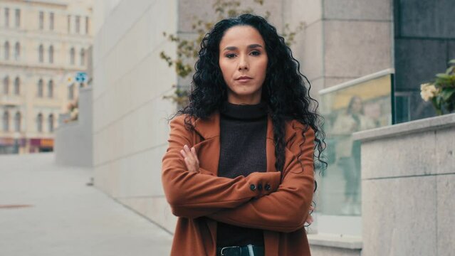 Caucasian Hispanic woman fashionable trendy girl lady turn turning around in city posing serious brunette student model tourist standing outdoors looking at camera arms crossed posing crossing hands