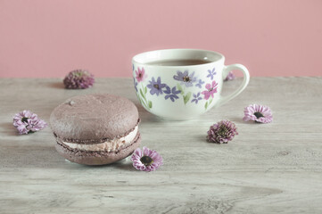 Macaroons and a cup of tea on a gray wooden table with scattered flowers. Selective focus, natural light