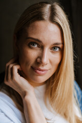 Blonde white woman smiling and looking at camera by window