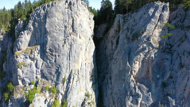 Two hikers, wife and husband, go over two steel bridges, one above other,  between two rocks on a via ferrata - 4k drone footage