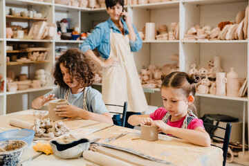 Female teacher talking on cellphone while working with kids in pottery class